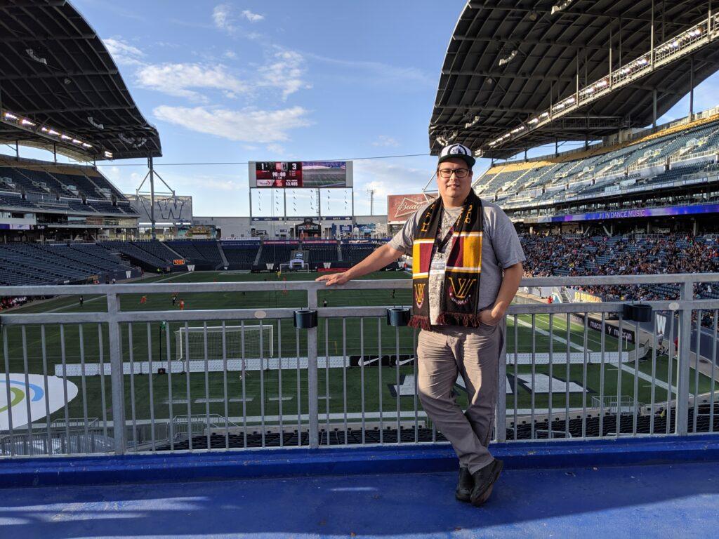 Jeremy 'scootR' standing at the end of Princess Auto Field in Winnipeg, with the football pitch and stands behind him.